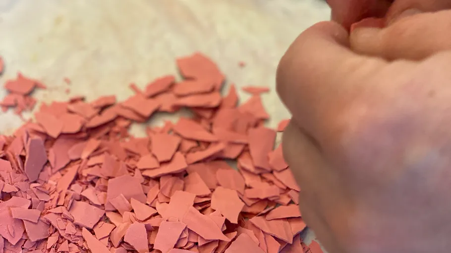 Person zerbröselt roten Ton in ihren Händen.