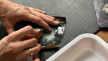 Hands peeling paper on work surface.