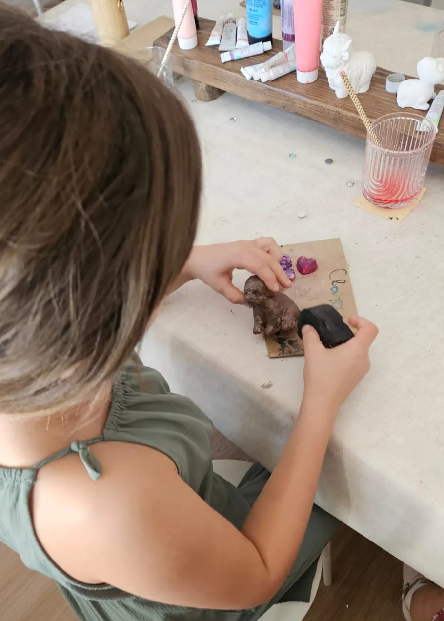Kind bemalt kleine Tonfigur am Tisch.