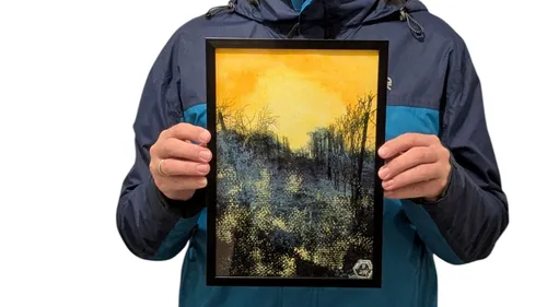 Person hält gerahmtes Kunstwerk eines Waldes.