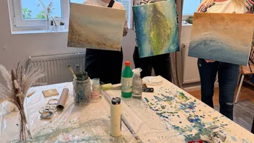 Three people holding abstract paintings indoors.