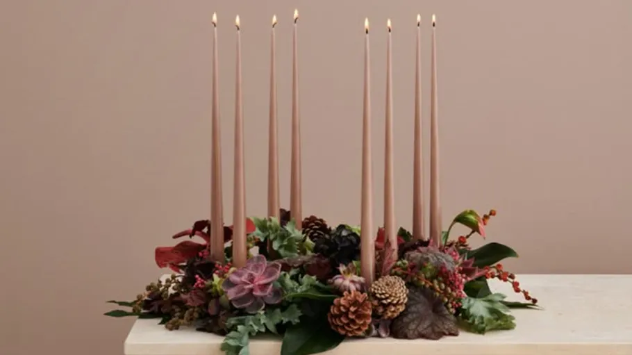 Tall candles in floral arrangement on table.