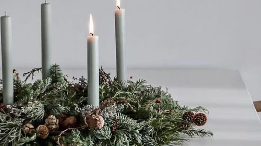 Candles in wreath on white table.