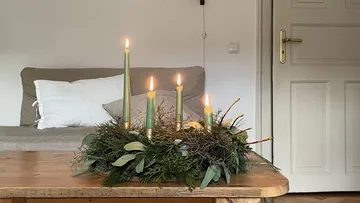 Candle wreath with five lit candles on table.