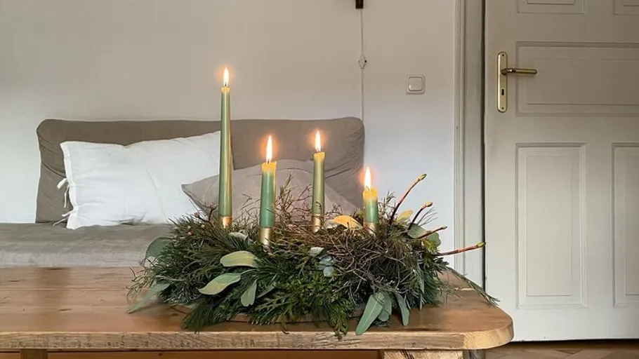 Kerzenkranz mit fünf brennenden Kerzen auf Tisch.