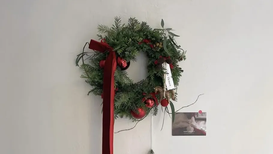 Wreath with red ornaments and ribbon on wall.