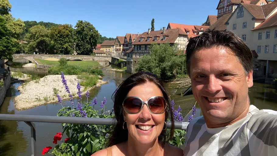 Couple smiling on bridge, river and buildings behind.