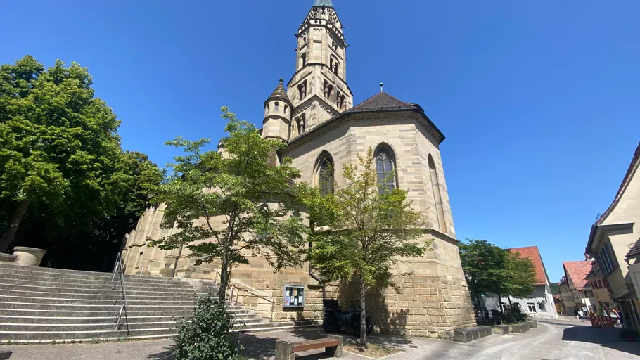 Steinerner Kirchturm mit Bäumen und blauem Himmel.