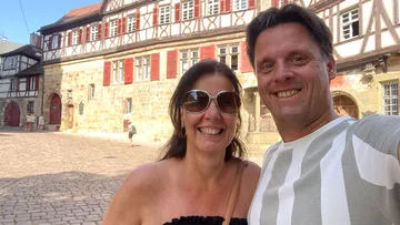 Smiling couple taking selfie in cobblestone courtyard.
