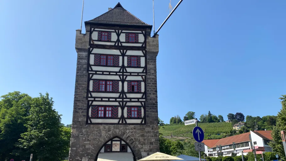 Mittelalterlicher Turm mit roten Fenstern, blauer Himmel.