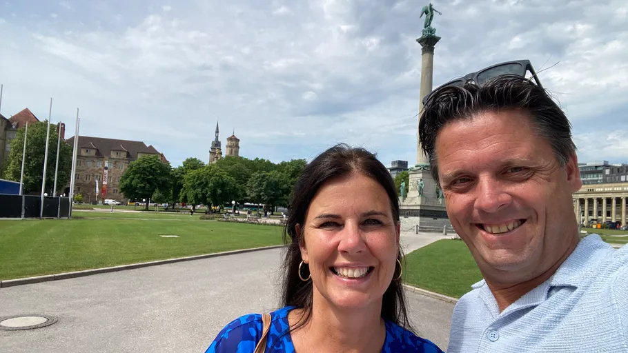 Zwei Personen lächelnd im Park mit Denkmal.