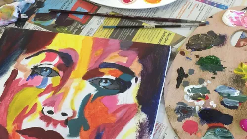 Colorful portrait painting with art supplies nearby.