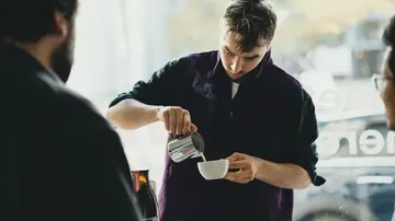 Barista pouring milk into a coffee cup.