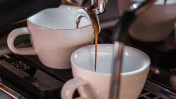 Two cups filling with espresso in machine.