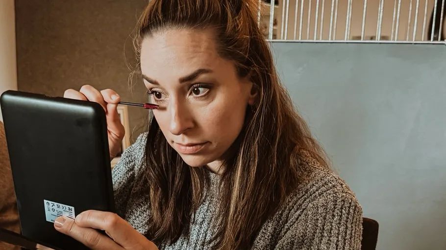 Frau trägt Make-up auf, hält Spiegel drinnen.