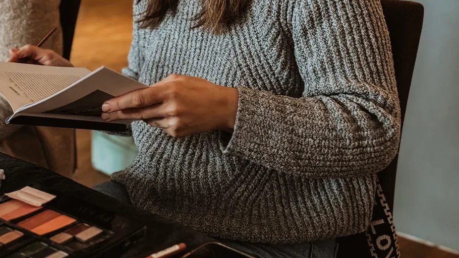Person reading book with makeup set nearby.