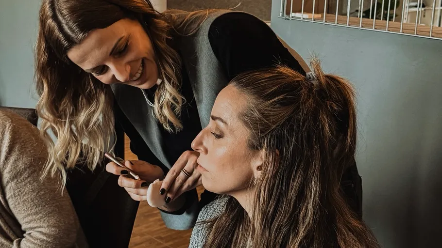 Woman showing phone to seated friend indoors.