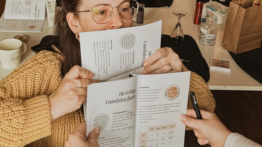 Person hält Makeup-Broschüre an einem Schreibtisch.