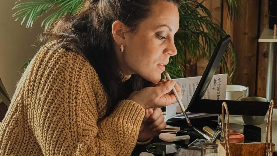 Frau trägt Make-up am Schminktisch auf.