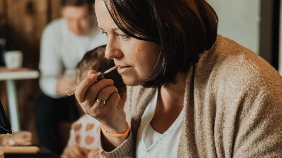 Woman applying lipstick indoors, sitting down.