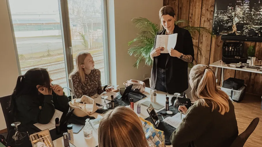 Woman teaching group at table with makeup items.