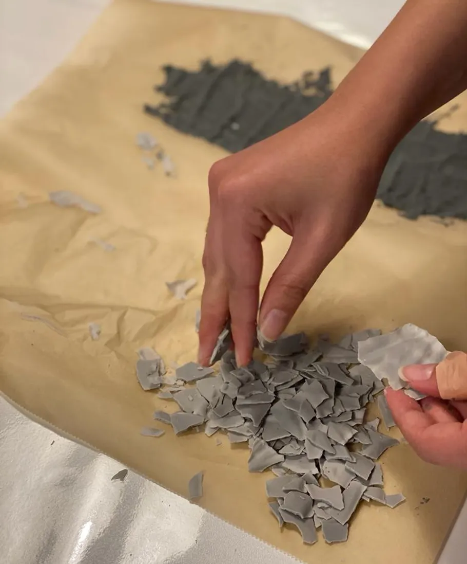 Hände sortieren graue Plastikfragmente auf Papier.