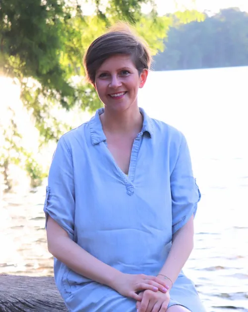 Frau sitzt an einem sonnigen See.