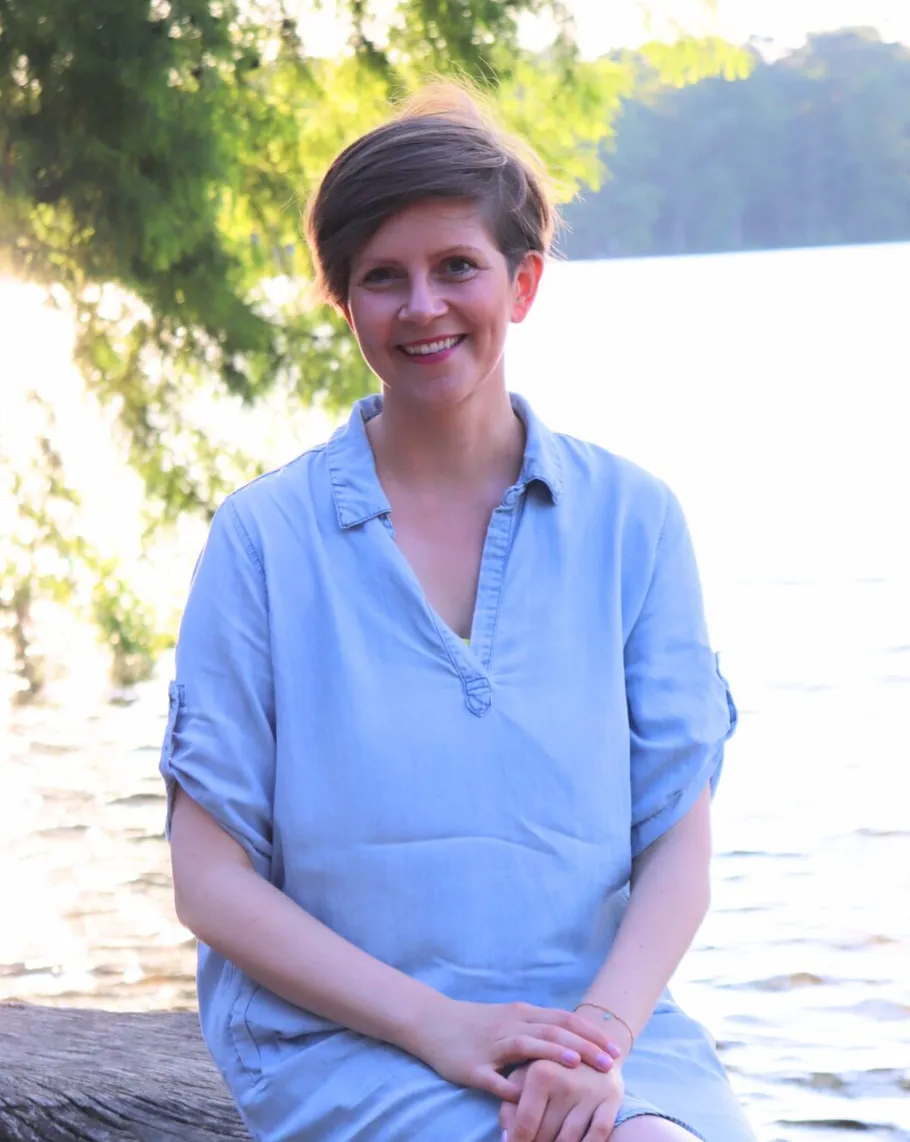 Woman sitting by a sunlit lake.
