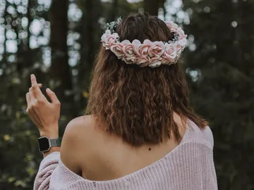 Woman with a wreath of flowers shows a finger in the forest.