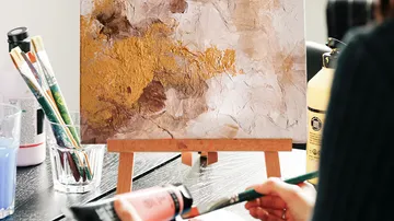 Abstract painting on easel with artist's hand.