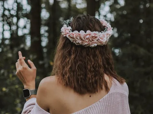 Woman with flower crown shows hand gesture in the forest.