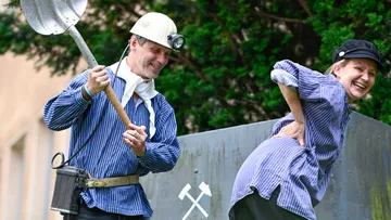 Zwei Personen in Bergbaukostümen, lachen im Freien.