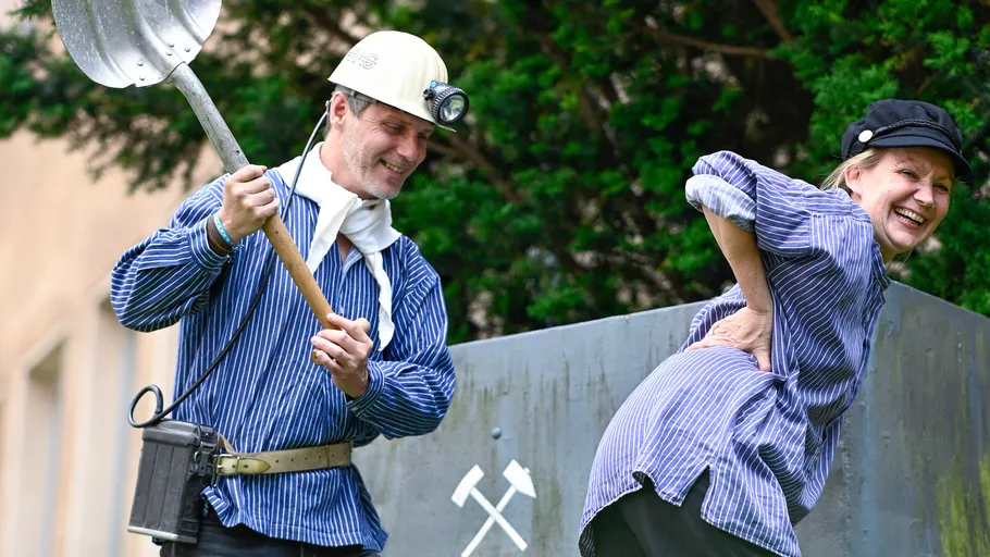 Zwei Personen in Bergbaukostümen, lachen im Freien.