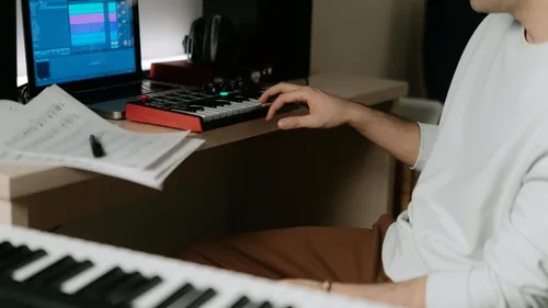 Person using MIDI controller at desk with computer.