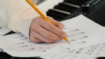 Hand schreibt auf Notenblatt neben Keyboard.
