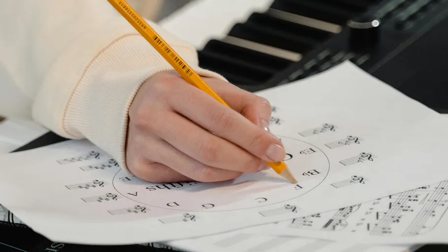 Hand schreibt auf Notenblatt neben Keyboard.
