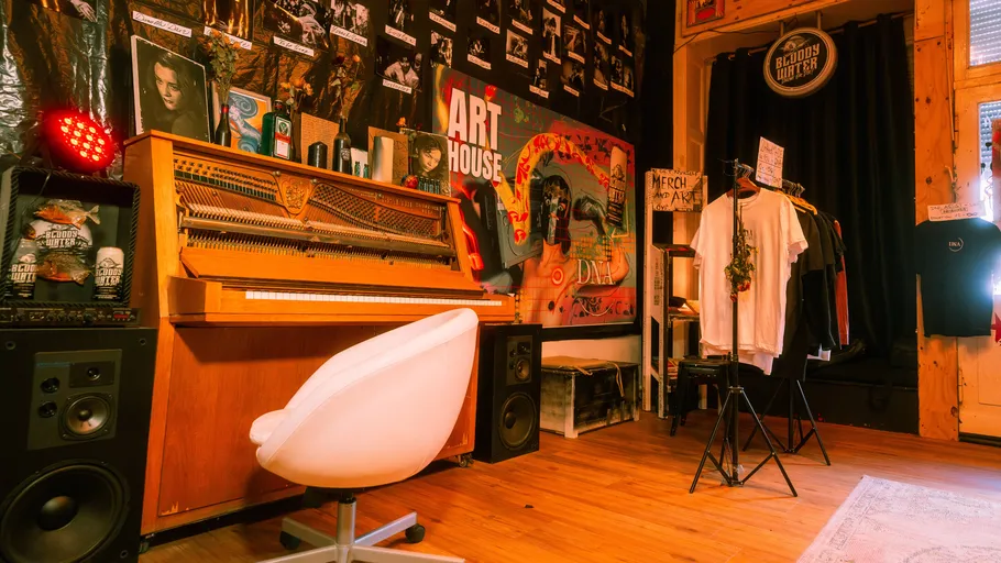 Room with piano, chair, posters, and clothes rack.