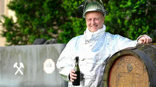Mann im Schutzanzug hält Flasche neben Fass.
