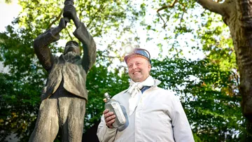 Man in mining attire holds trophy outdoors.