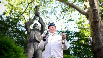 Man in white coat holds beer and lamp outdoors.