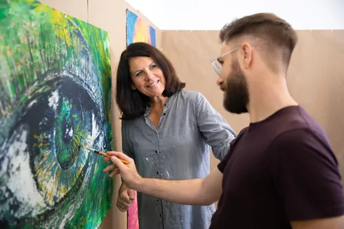 Two people discussing a colorful eye painting.