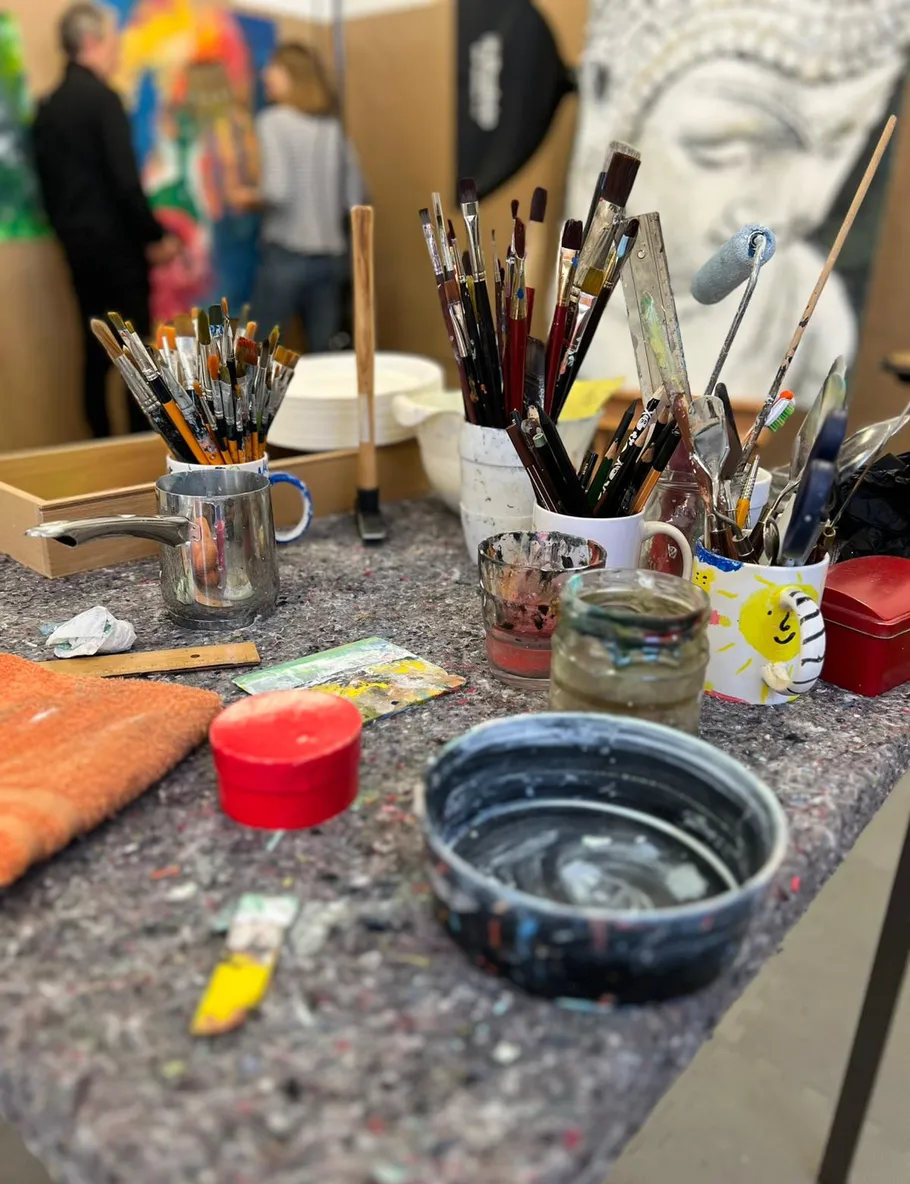 Paintbrushes on table, artists in studio background.