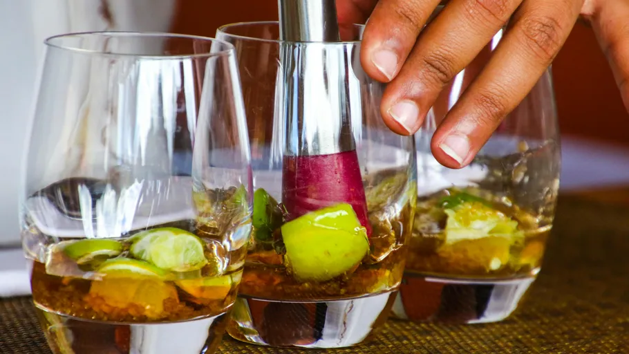 Hand muddling limes in three glasses.
