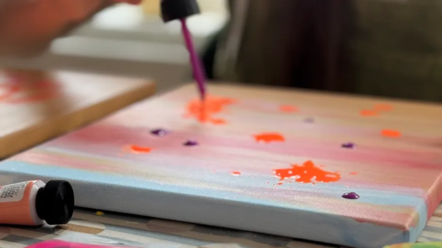 Hand trägt Farbe auf eine bunte Leinwand auf.