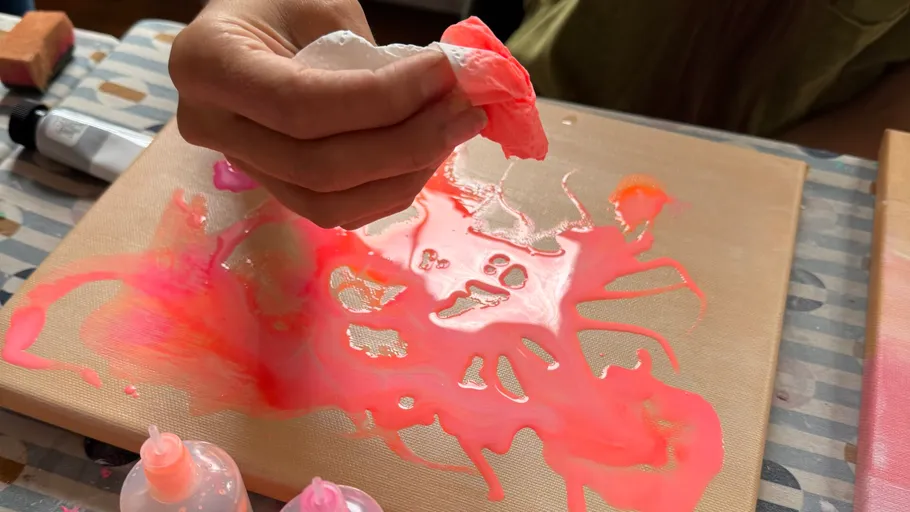 Hand wipes pink paint on canvas.