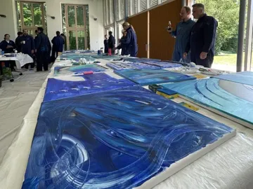 Blue paintings are lying on a table, people are looking at them.