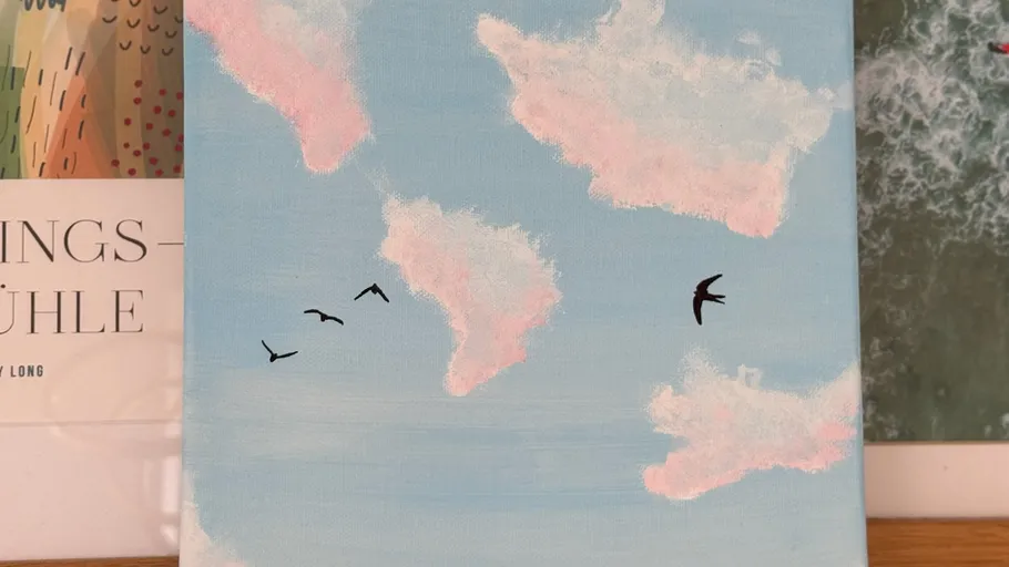 Birds flying under pink clouds, blue sky.