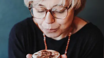 Frau bläst auf schaumige Kaffeetasse.