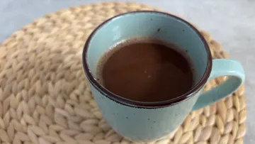 Blue mug with hot beverage on woven mat.