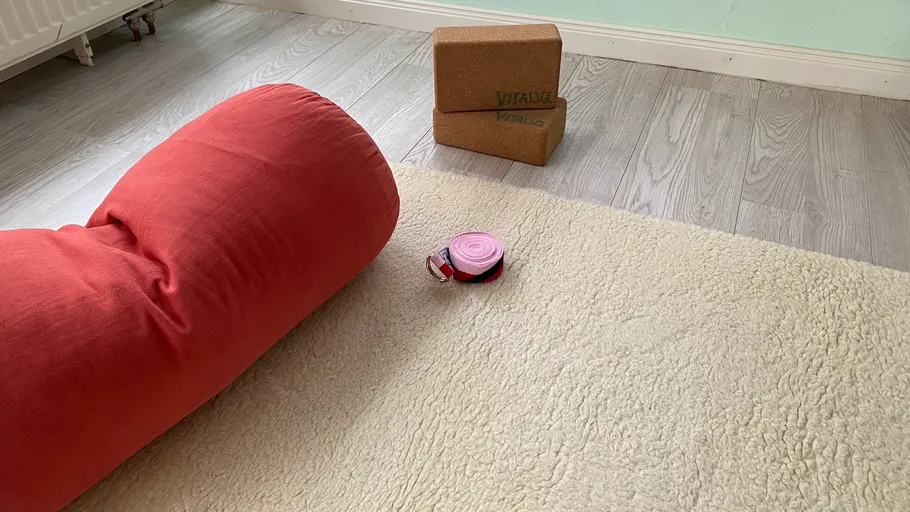 Yoga-Bolster, Blöcke, Gurt auf Matte im Raum.